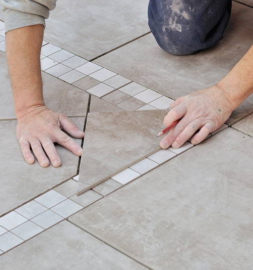 Pose de carreaux de sol en grès cérame, un artisan utilise un crayon pour marquer une coupe près d'une bordure en mosaïque claire.